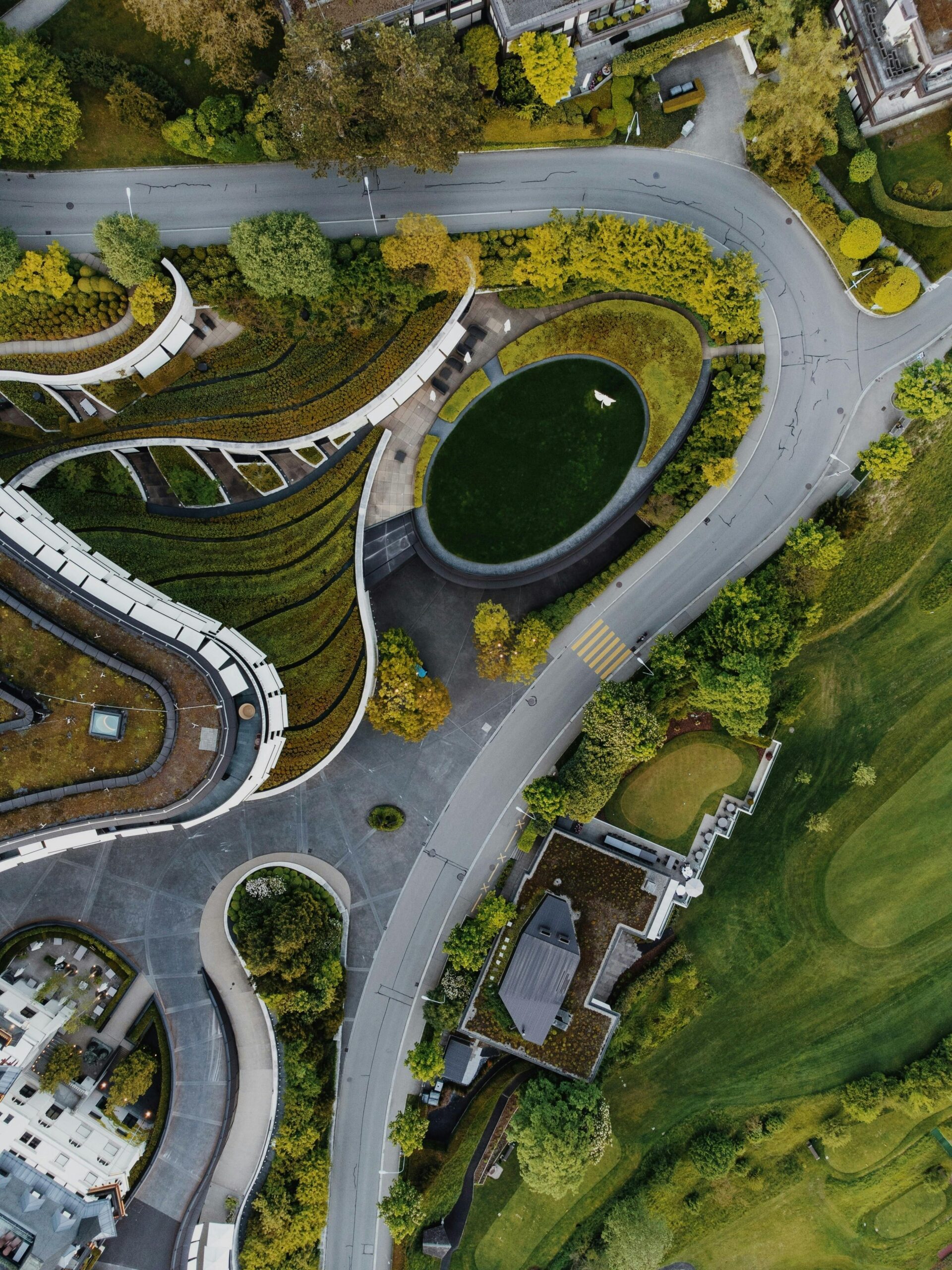 Widok z lotu ptaka na nowoczesną architekturę otoczoną zielenią, z krętymi ścieżkami i ogrodami w miejskim krajobrazie.
