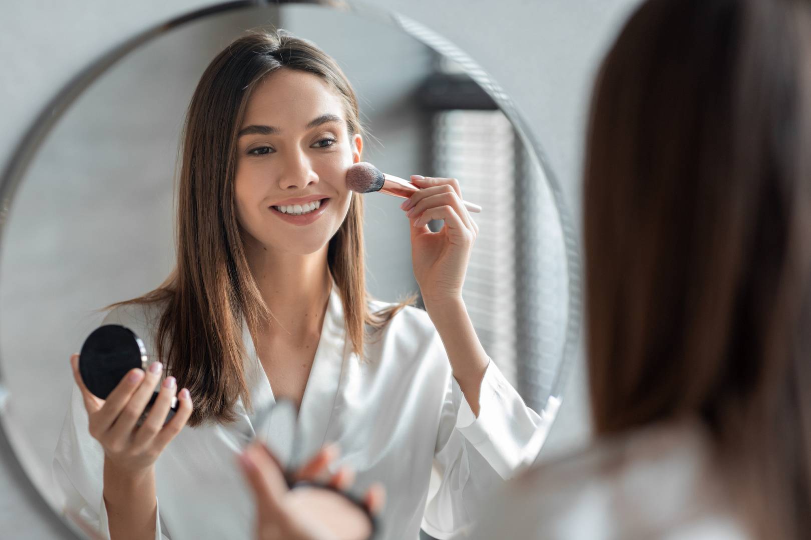 Attractive Young Woman Doing Daily Makeup While Standing Near Mirror In Bathroom